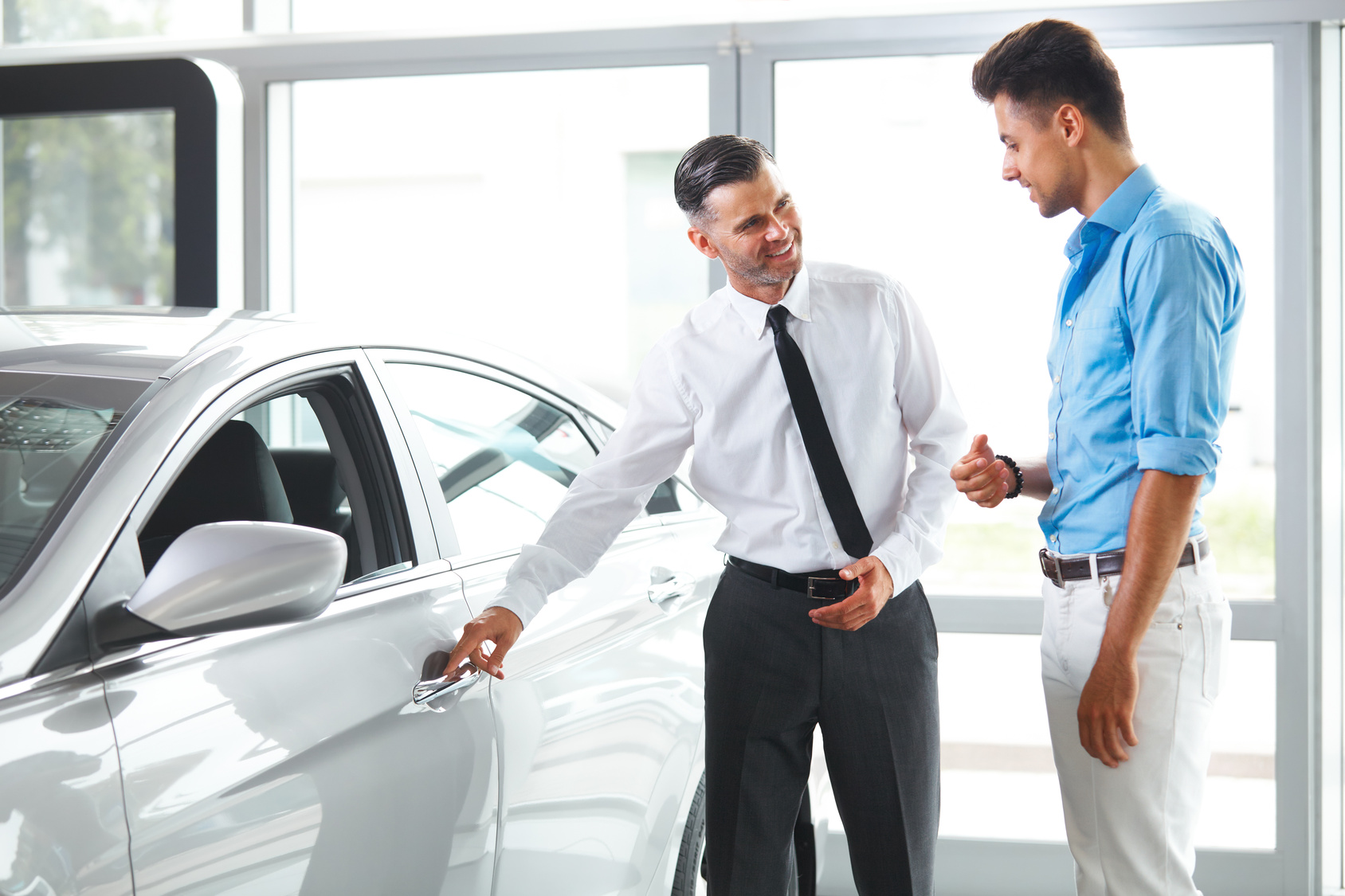 Car Sales Consultant Showing a New Car to a Potential Buyer in Showroom