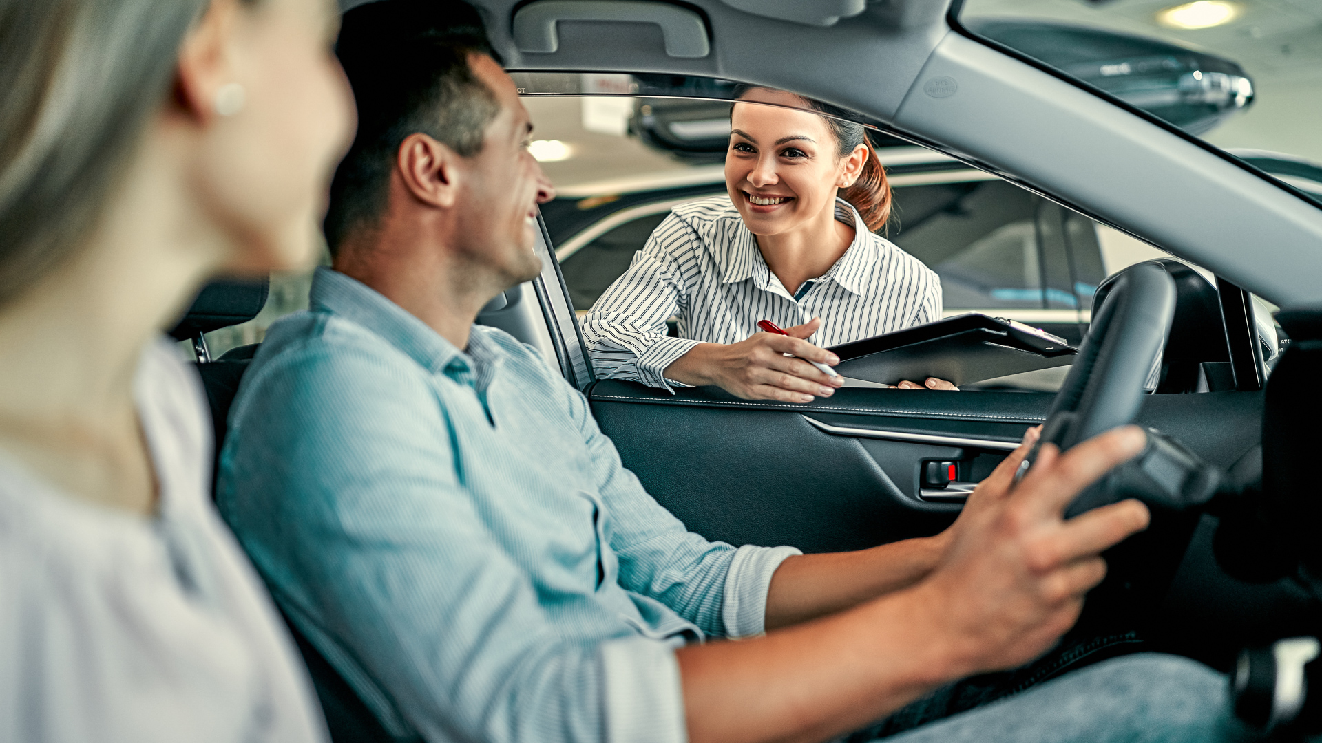 Young female consultant and couple buyers sitting in new car signing contract in auto show. Concept for car rental.